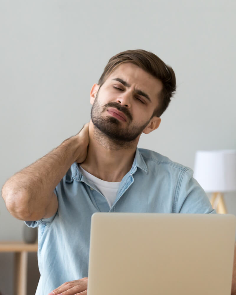 man set in front of laptop rubbing his back of head